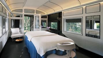 Ein modernes, helles Schlafzimmer mit Bett, Sitzecke und großen Fenstern mit Blick auf Grünflächen.
