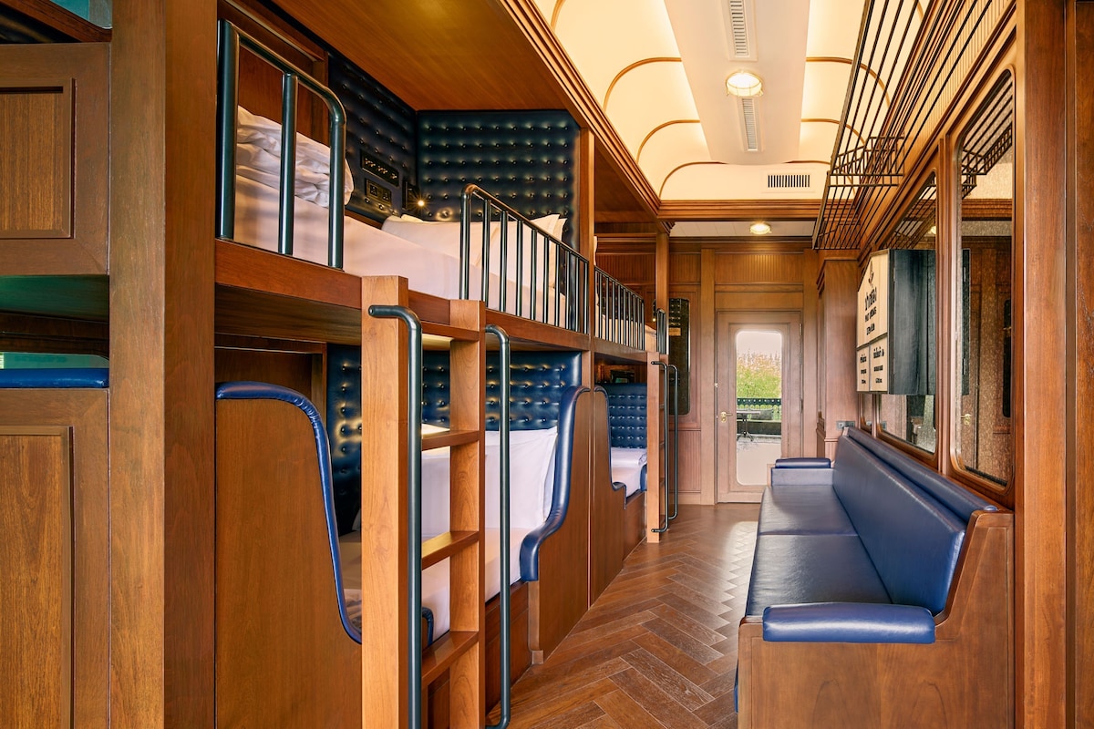 A train carriage with wooden walls, a herringbone floor, and a bench along the right side.