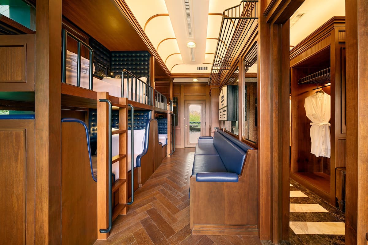A hallway with wooden flooring, a blue bench, and a wardrobe with hanging clothes.