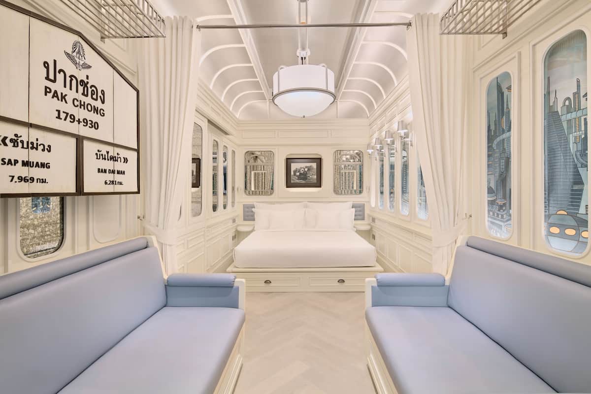 A room with a bed, two blue sofas, a chandelier, and a cityscape view through the windows.