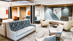 Un hall d’hôtel moderne avec un plafond haut, un espace de détente central agrémenté de canapés et de fauteuils, et une grande œuvre d’art abstraite qui orne un mur.