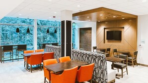 Un espace repas moderne avec des chaises orange, des tables en bois et une grande fenêtre donnant sur un paysage aux motifs bleus.