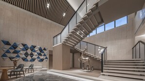 A spacious lobby with a modern staircase, a geometric wall art installation, and a seating area with a table and chairs. - Holiday Inn Express Tengchong Hot Spring by IHG (Baoshan)