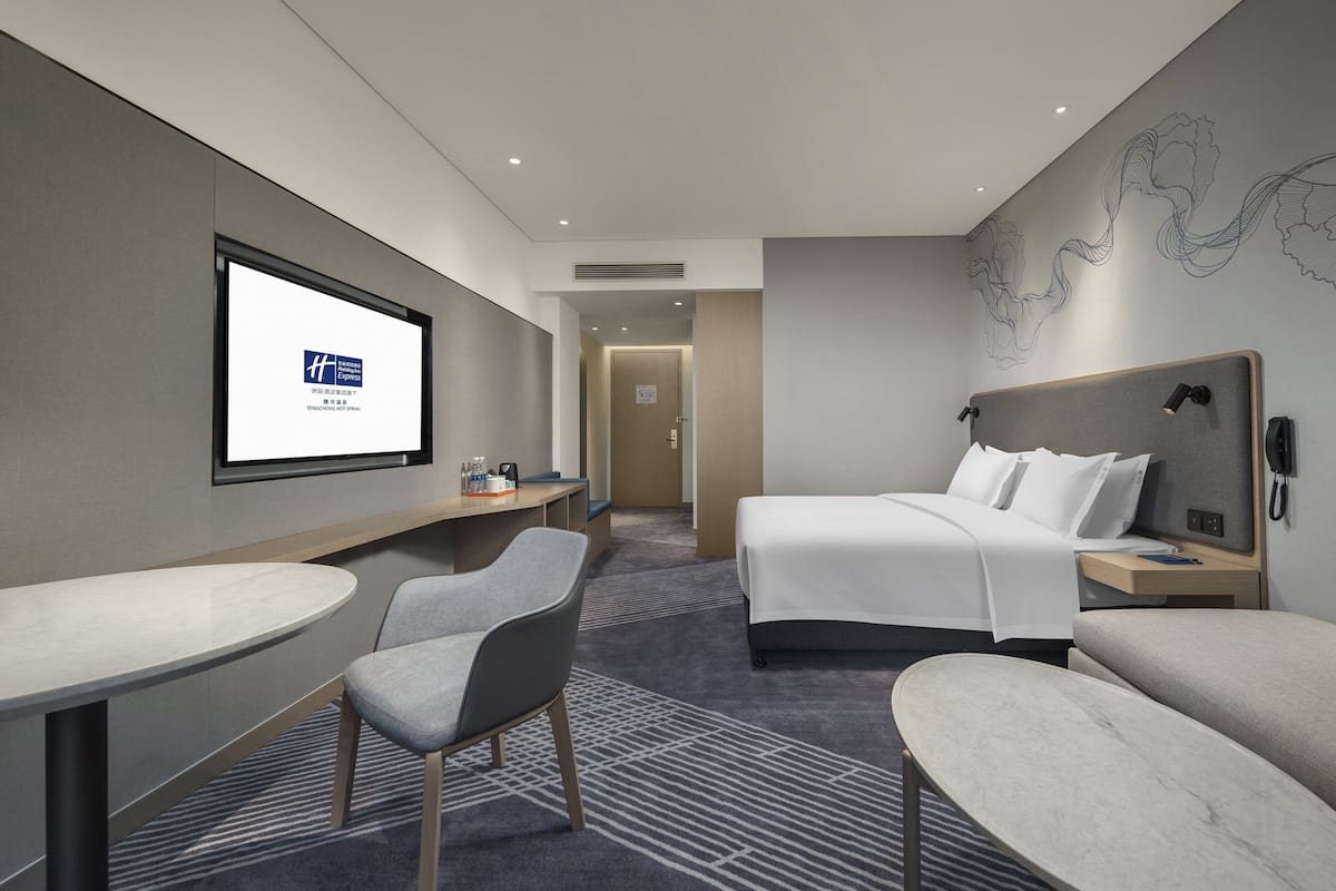A modern hotel room with a bed, a desk, a chair, and a sofa.