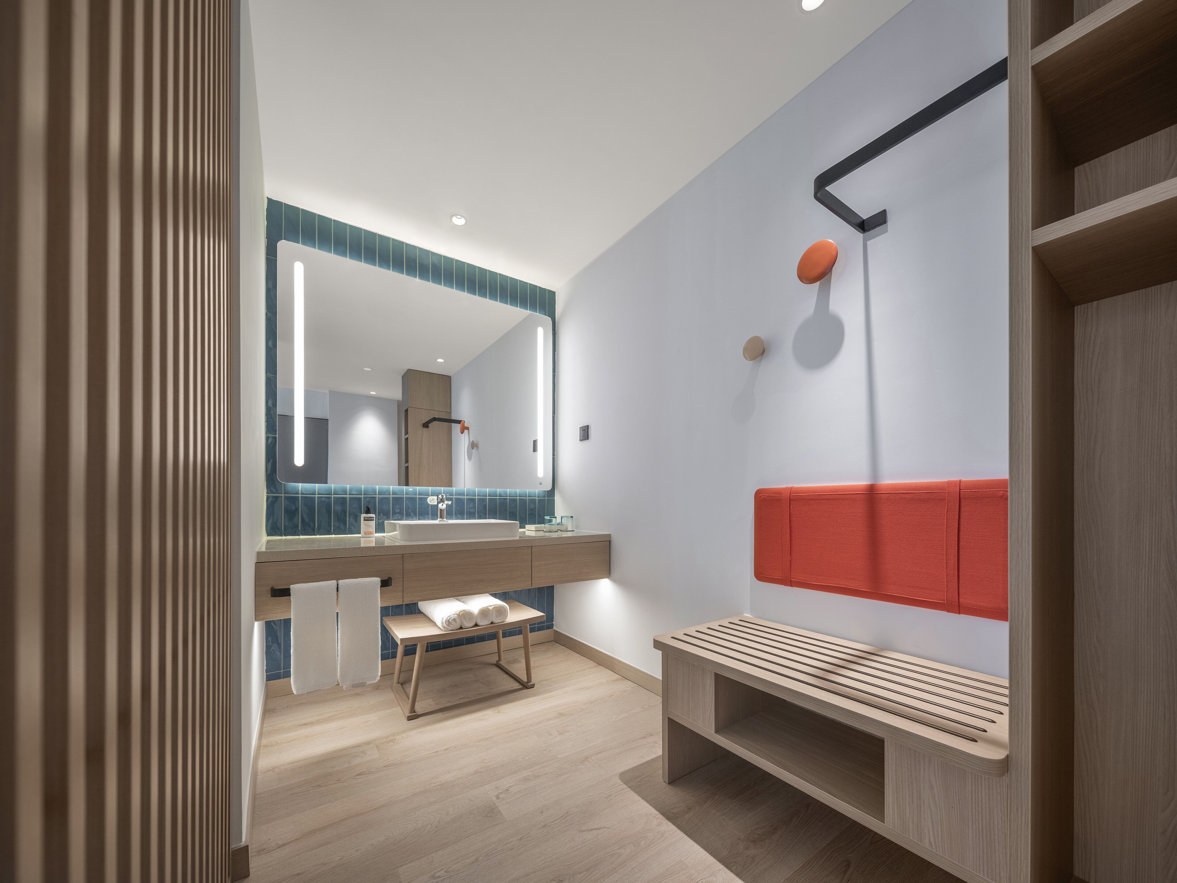 A modern bathroom with a large mirror, a bench, and a shower area.