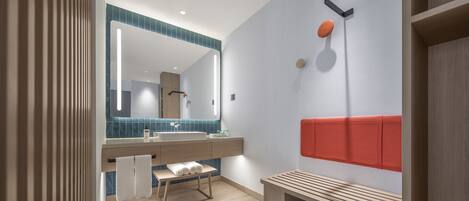A modern bathroom with a large mirror, a bench, and a shower area.