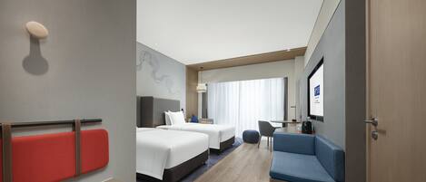 A hotel room with two beds, a seating area, a TV, and a wooden floor.