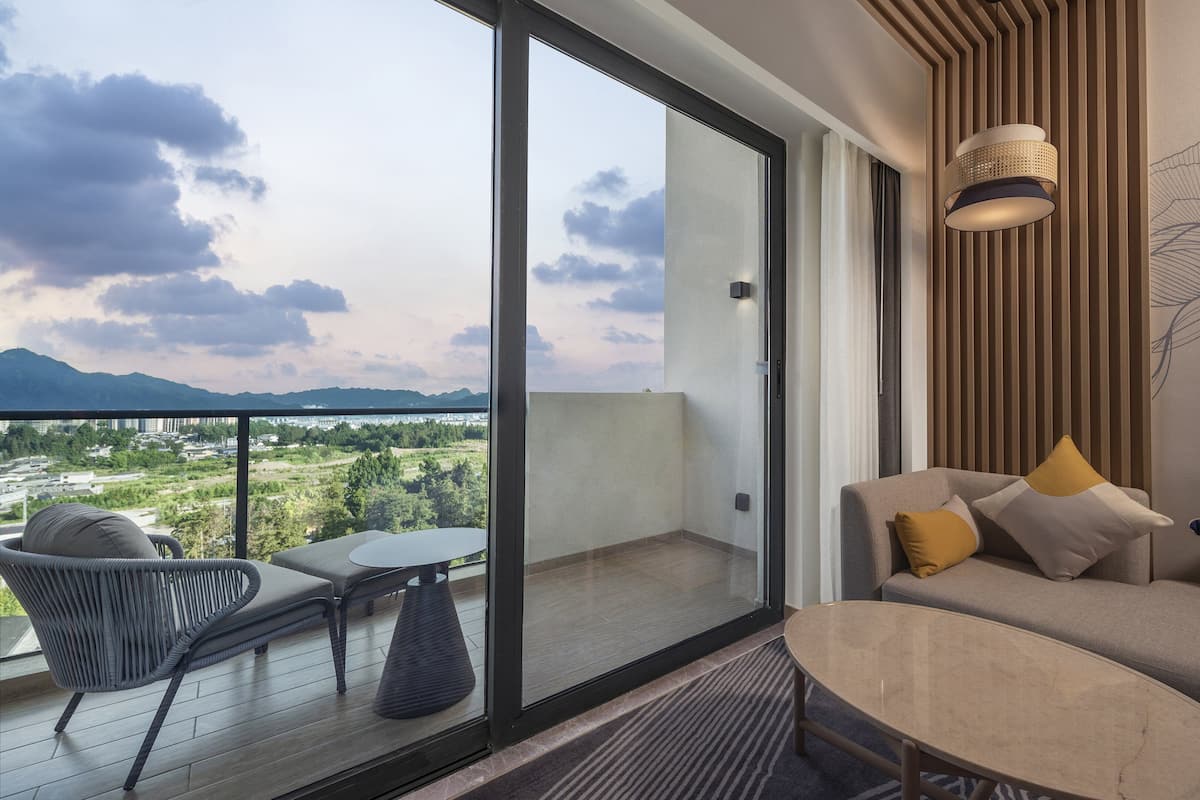 A balcony with a sofa and chairs, a table, and a view of a cityscape and mountains.
