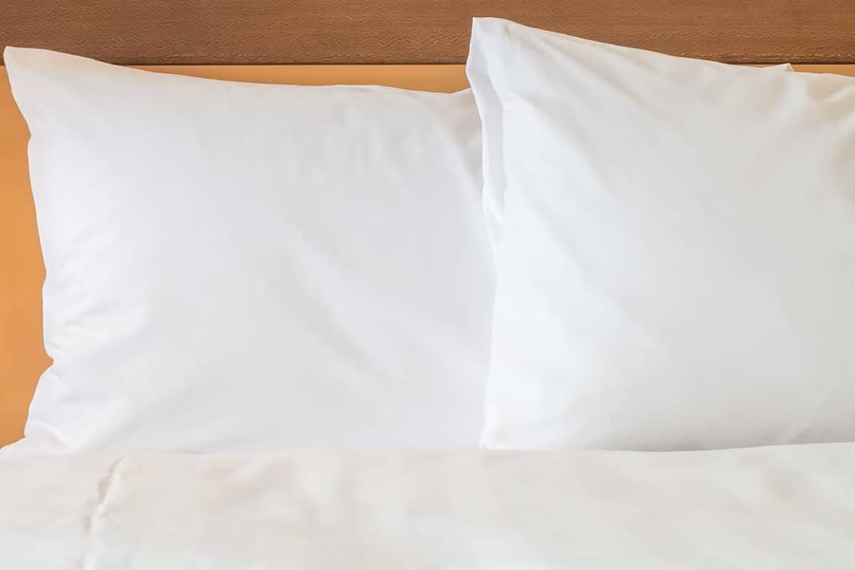 A bed with white bedding and pillows against a wooden headboard.