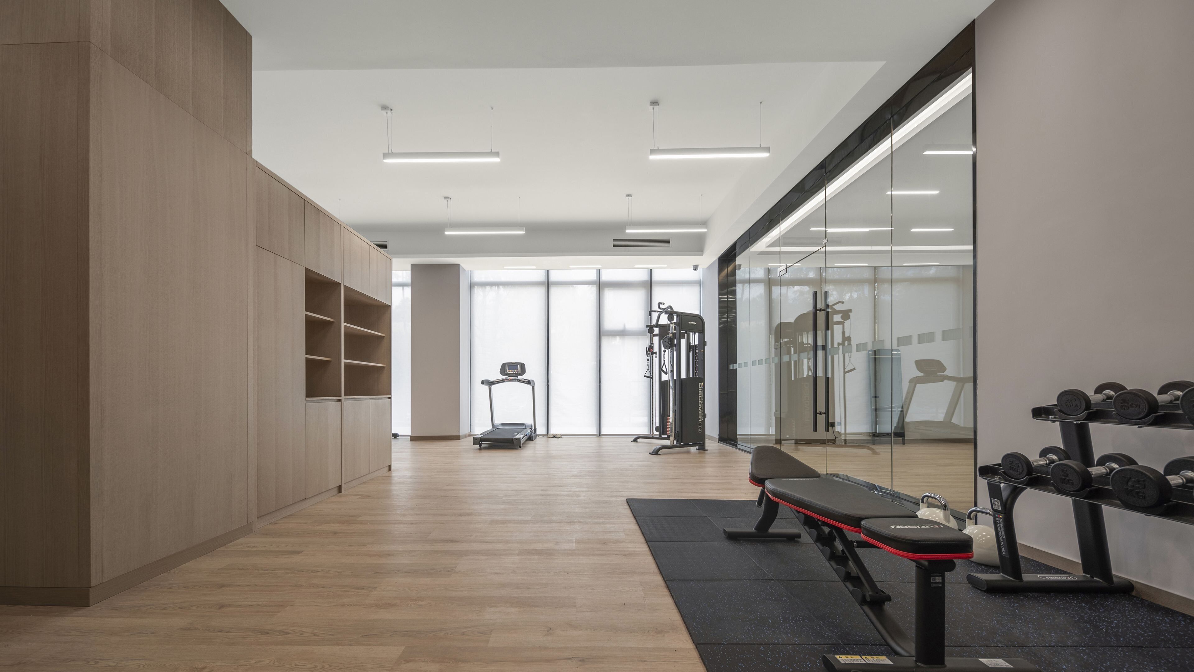 Academia moderna com piso de madeira, equipamentos de ginástica e espelho grande na parede.