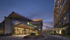 A modern hotel with a glass facade, a landscaped garden with flowers, and a sign for Holiday Inn Express. - Holiday Inn Express Tengchong Hot Spring by IHG (Baoshan)