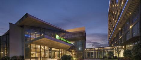 A modern hotel with a glass facade, a landscaped garden with flowers, and a sign for Holiday Inn Express.