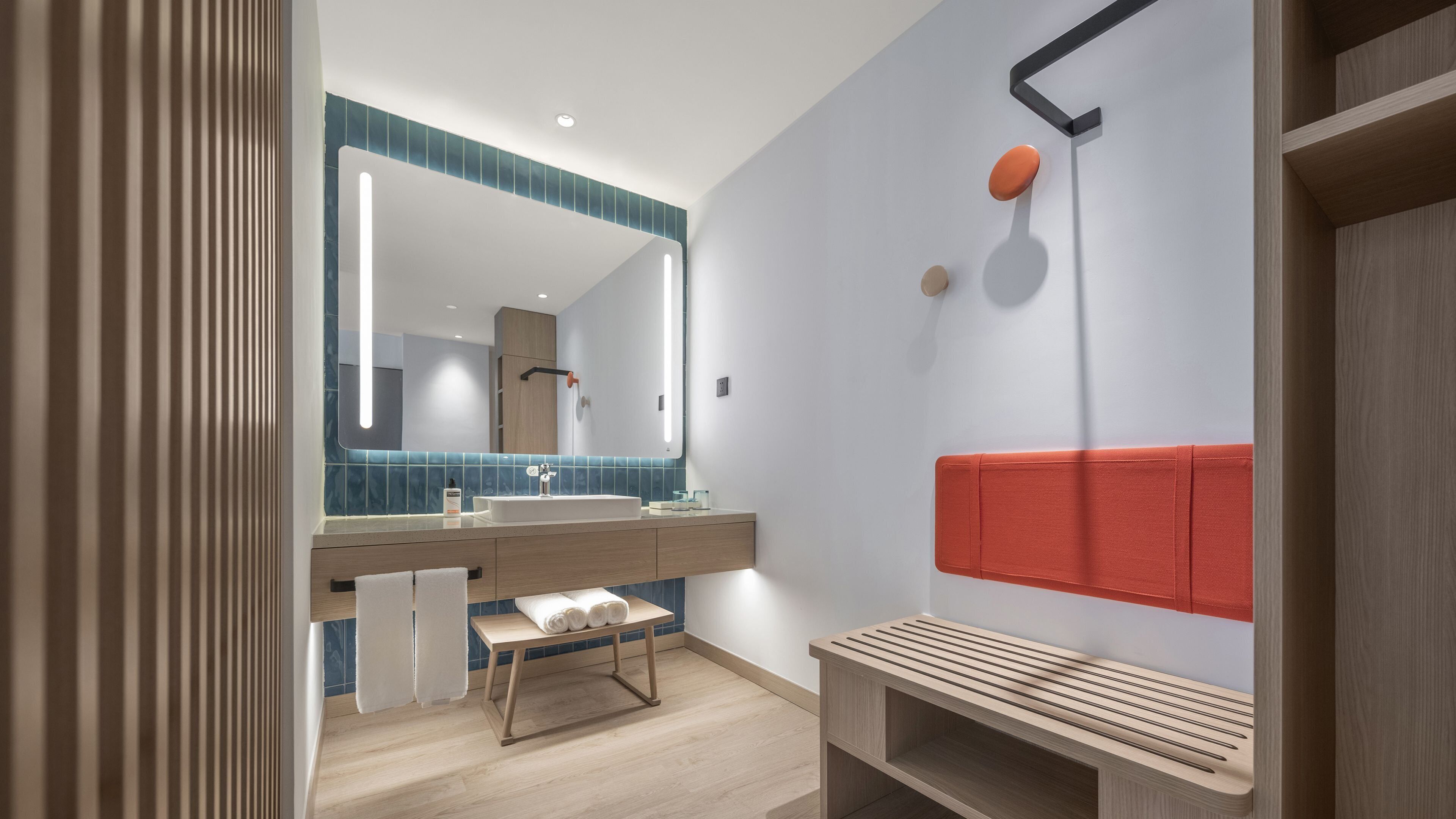A modern bathroom with a large mirror, a shower, and a bench.