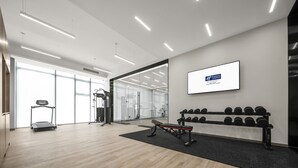 A modern gym with exercise equipment, a treadmill, and a wall-mounted screen displaying a logo.