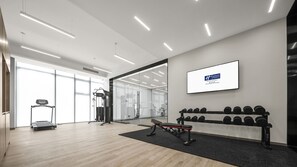 A modern gym with exercise equipment, a treadmill, and a wall-mounted screen displaying a logo.