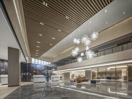 A spacious lobby with a high ceiling, modern lighting fixtures, and a central seating area.