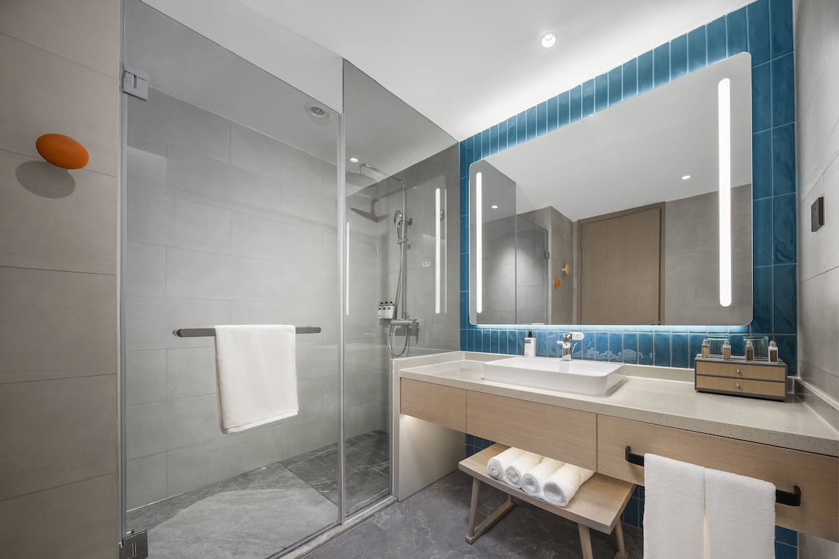 A modern bathroom with a glass shower enclosure, a large mirror, and a vanity with a sink and towel rack.