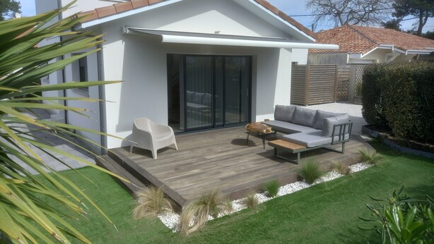 A modern house with a patio, a sliding glass door, a grey sofa, and a wooden deck. - Contemporary villa, 5' town center and beach 10 minutes by bike. (Capbreton)