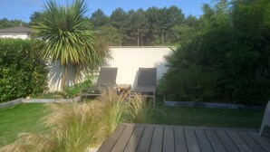 A wooden deck with two lounge chairs, surrounded by lush greenery and a white wall in the background. - Contemporary villa, 5' town center and beach 10 minutes by bike. (Capbreton)