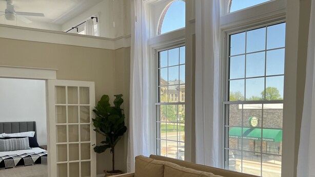 A living room with a beige sofa, a wooden coffee table, and a large window with curtains.