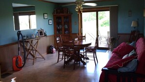 A spacious living room with a dining area, a ceiling fan, and a large window allowing natural light.