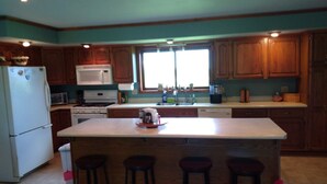 A kitchen with wooden cabinets, a white refrigerator, a microwave, a stove, and a sink. There are four stools around the island.