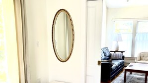 A bedroom with a large bed, a bedside table, a mirror, a window with curtains, a sofa, and a coffee table. - Spacious and Historic Downtown Home 1 minute walk from the ocean. (Bar Harbor)