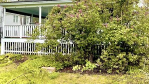 A two-story white house with a covered porch and a white picket fence. - Spacious and Historic Downtown Home 1 minute walk from the ocean. (Bar Harbor)