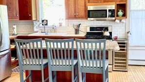 A kitchen with wooden cabinets, a central island with chairs, a microwave, and a stove. - Spacious and Historic Downtown Home 1 minute walk from the ocean. (Bar Harbor)