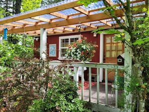 A wooden deck with a pergola, a hanging flower basket, and a birdhouse.