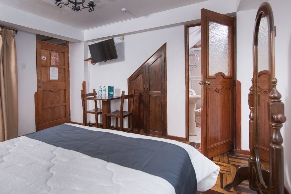 Un dormitorio con cama, armario de madera, televisión y espejo.
