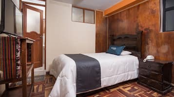 A bedroom with a bed, wooden headboard, a bedside table with a phone, a bookshelf, and a patterned floor.