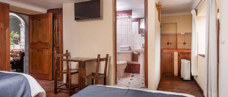A hotel room with two beds, a wooden desk, a chair, a TV, and a bathroom visible through an open door.
