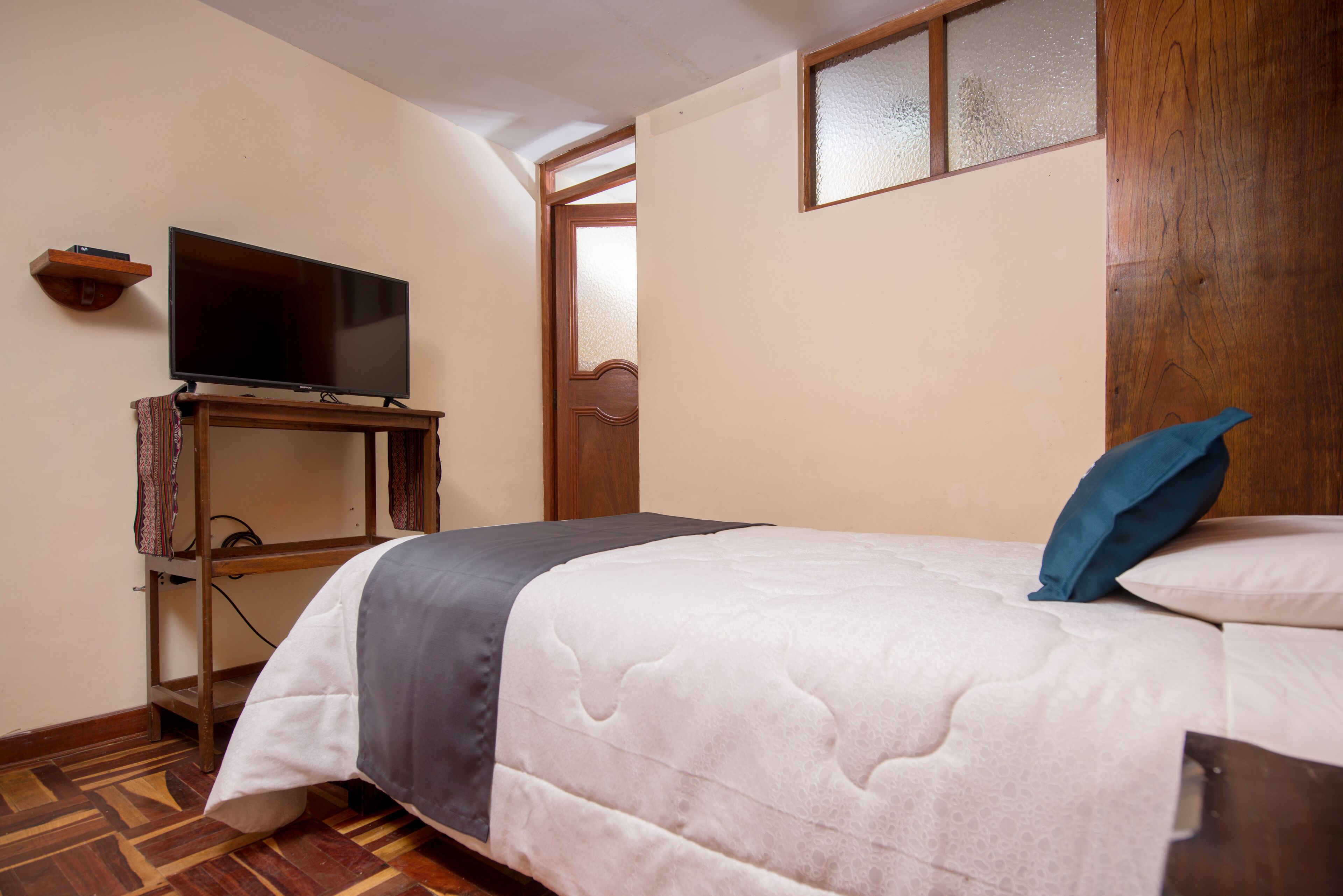 A bedroom with a bed, a television on a wooden stand, and a door with frosted glass panels.