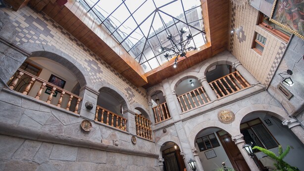 Un atrium à plusieurs niveaux, agrémenté d’arcs en pierre, de balcons en bois et d’une verrière.