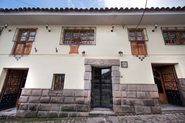 Un edificio con fachada de piedra, múltiples ventanas con rejas metálicas y una entrada central con puerta.