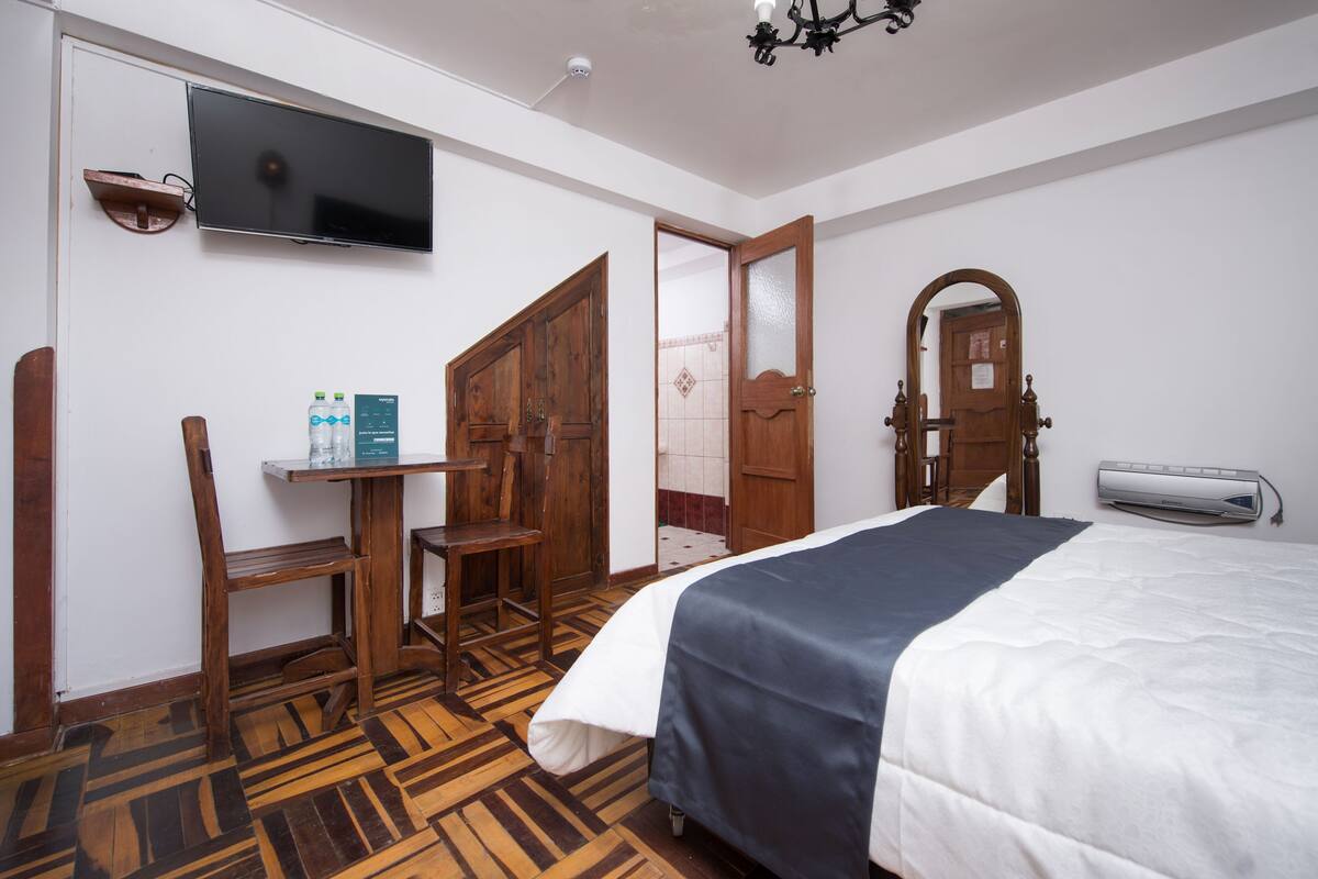 Habitación de hotel con una cama, un escritorio con silla, televisor y espejo.