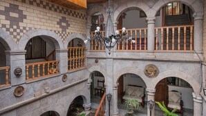 Un bâtiment en pierre à plusieurs niveaux, doté de balcons, d’un lustre et d’une fontaine.