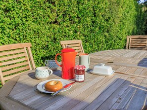 Ein runder Holztisch mit einer Speisenplatte, einer roten Kaffeekanne, einem Marmeladenglas und einem weißen Behälter.