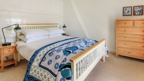 Ein Schlafzimmer mit einem Bett, Nachttischen, einer Hängelampe, einer hölzernen Kommode und zwei Bildern an der Wand.