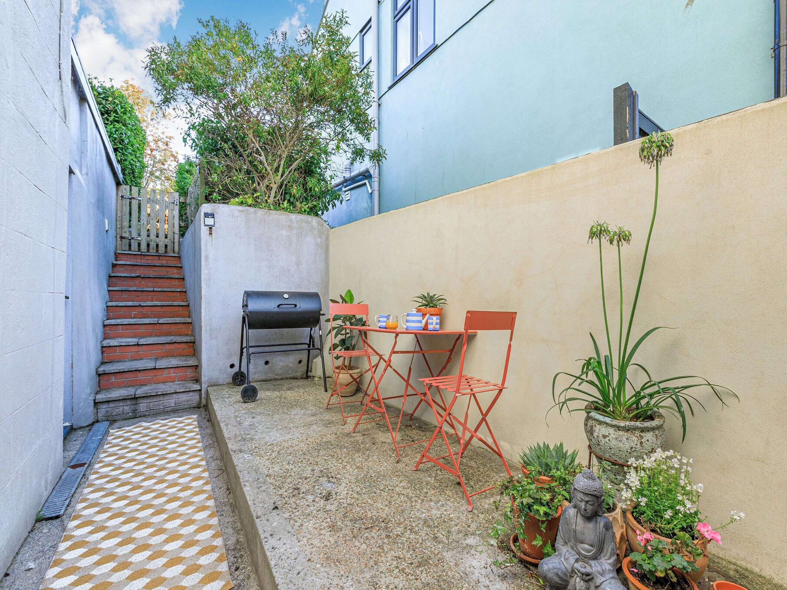 A small outdoor patio with a grill, a table with chairs, and potted plants.