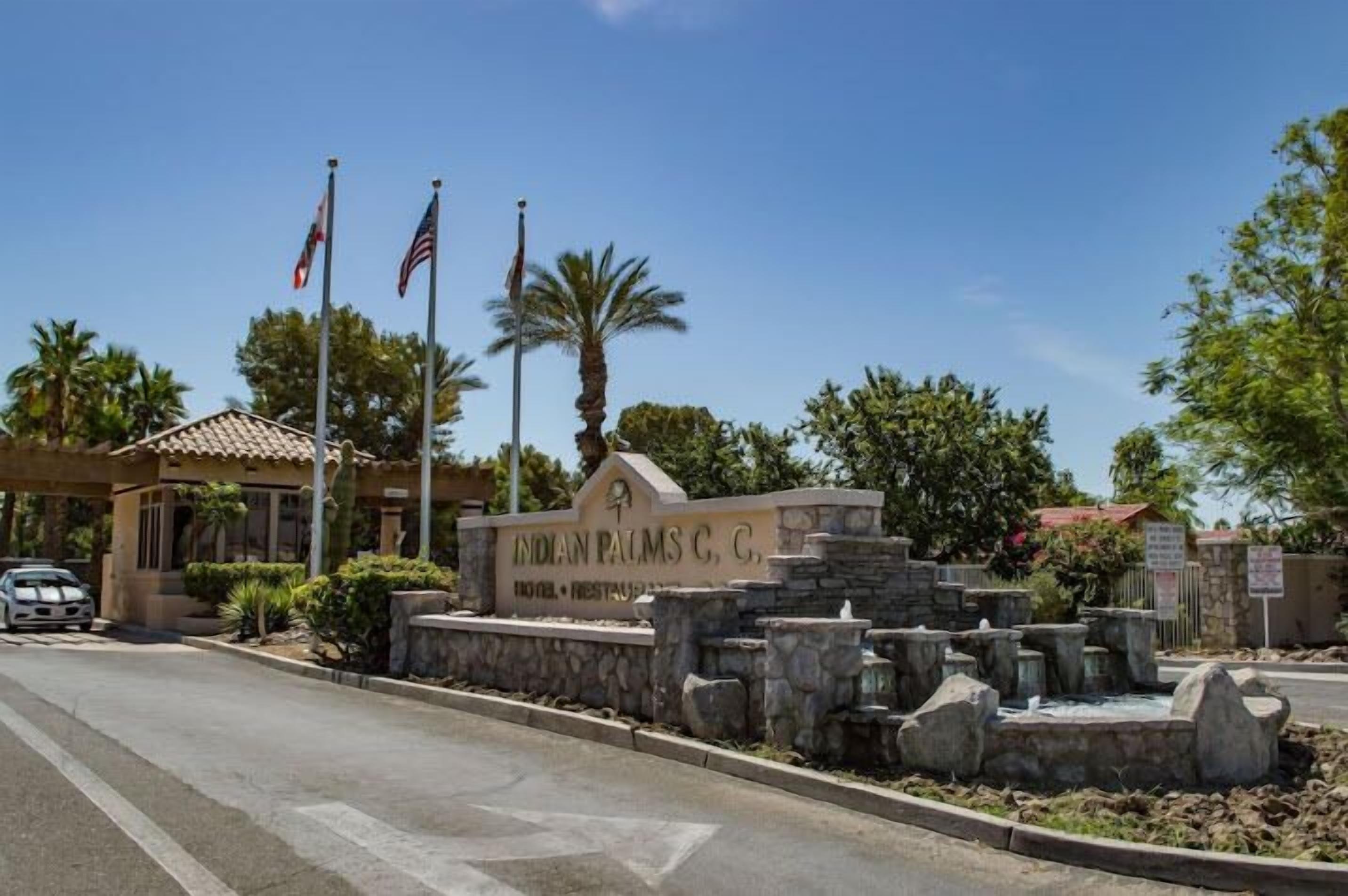 A sign for Indian Palms C, C, with a stone wall and palm trees.