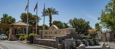 A sign for Indian Palms C, C, with a stone wall and palm trees.