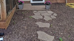 Una casa con puerta principal, dos macetas, un camino de piedra y un jardín.