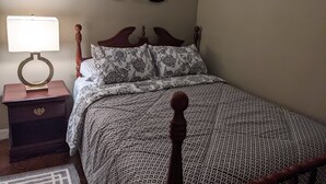 Un dormitorio con cama, mesita de noche, lámpara y barcos decorativos en la pared.