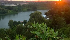 Une vue panoramique d’un lac entouré d’une végétation luxuriante et de collines, au coucher du soleil.
