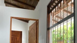 Un couloir avec une porte en bois et une fenêtre ornée d’une grille métallique.