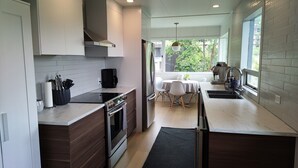 A modern kitchen with a central island, built-in oven, and a coffee machine. - Modesta Winery Guest House (Naramata)