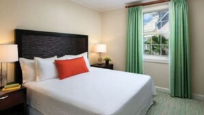Een hotelkamer met een groot bed, een nachtkastje met een lamp en een raam met groene gordijnen.