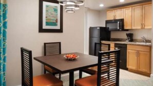 A dining area with a table and four chairs, a black refrigerator, wooden cabinets, and a framed picture on the wall. - Harborside Atlantis Sleeps 4 (Paradise Island)